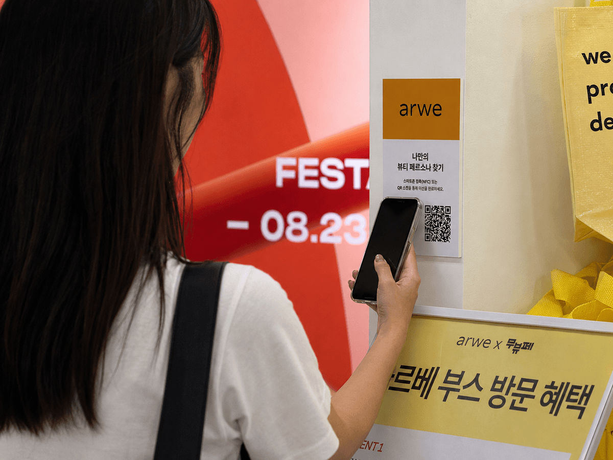 A MUSINSA Beauty Festa visitor holding a smartphone to the NFC and QR sign at a brand booth